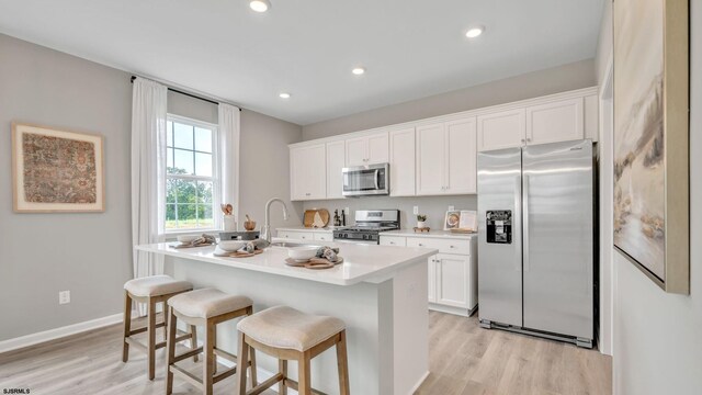 kitchen with sink, a breakfast bar area, white cabinetry, an island with sink, and stainless steel appliances