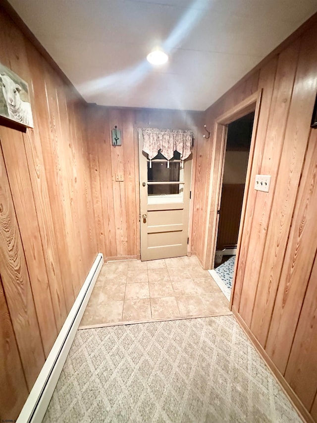 hallway with wood walls, a baseboard radiator, and light carpet