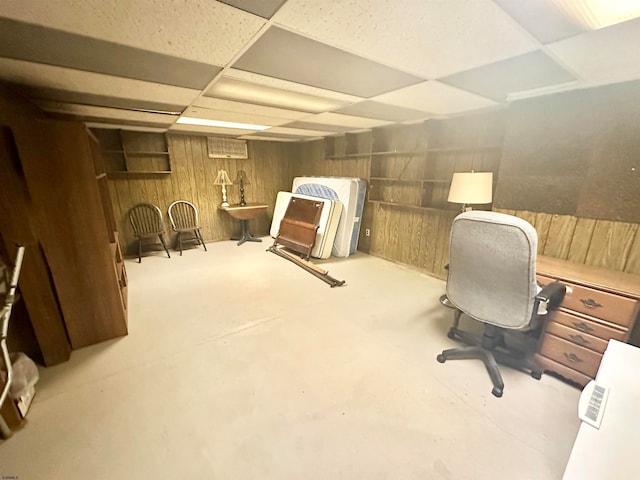 office area featuring concrete floors, a drop ceiling, and wood walls