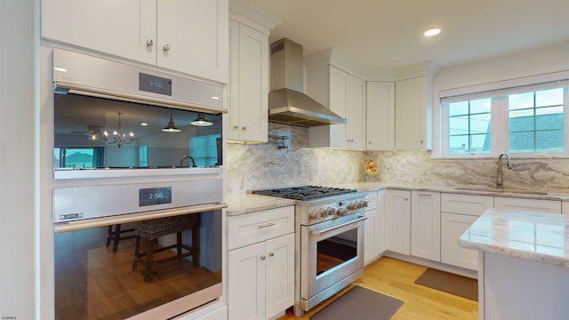 kitchen with sink, wall chimney range hood, light hardwood / wood-style floors, high end stainless steel range, and white cabinets