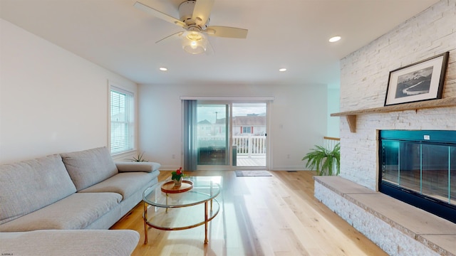 living room featuring ceiling fan, a fireplace, and light wood-type flooring