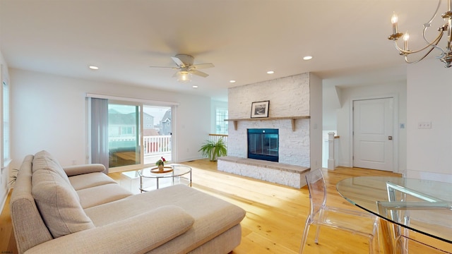 living room featuring a fireplace, wood-type flooring, and ceiling fan with notable chandelier