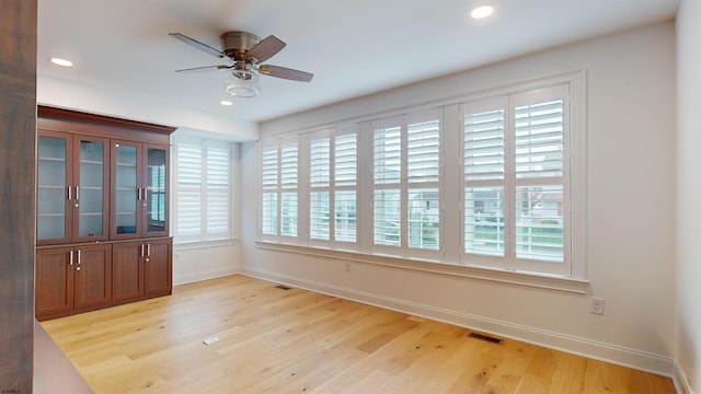 empty room with ceiling fan, plenty of natural light, and light hardwood / wood-style floors