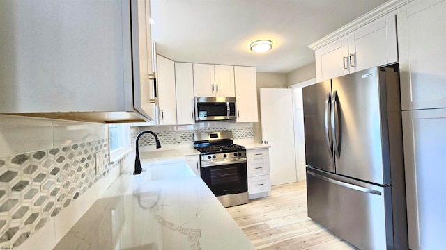 kitchen with backsplash, white cabinets, sink, light stone countertops, and appliances with stainless steel finishes