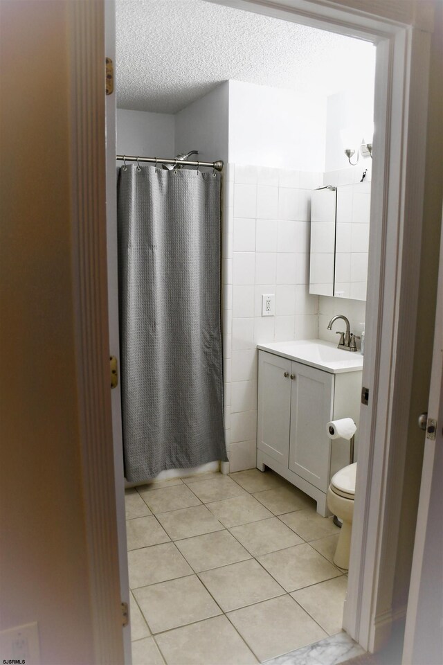 bathroom featuring a shower with shower curtain, tile patterned floors, vanity, a textured ceiling, and tile walls