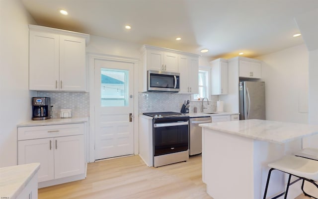 kitchen featuring white cabinets, backsplash, light hardwood / wood-style floors, and stainless steel appliances