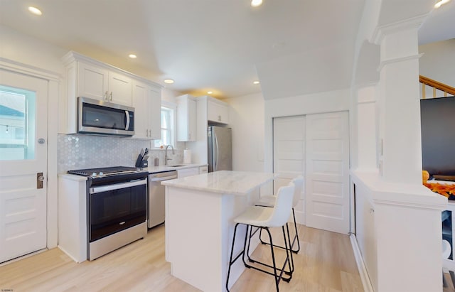 kitchen with white cabinets, sink, light hardwood / wood-style floors, a kitchen island, and stainless steel appliances