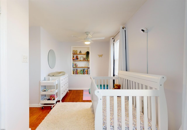 bedroom with wood-type flooring, a nursery area, and ceiling fan