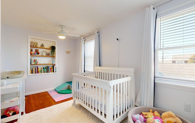 bedroom with hardwood / wood-style flooring, ceiling fan, a crib, and multiple windows