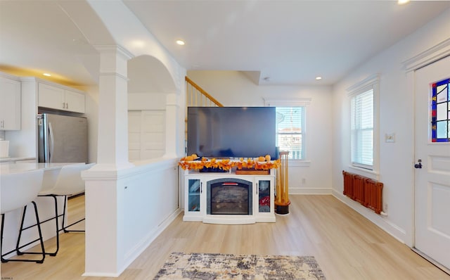 living room featuring radiator heating unit, decorative columns, and light hardwood / wood-style flooring