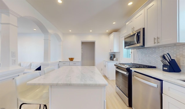 kitchen with a kitchen bar, appliances with stainless steel finishes, light stone counters, light hardwood / wood-style flooring, and white cabinets