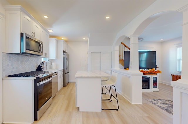 kitchen featuring white cabinetry, a center island, stainless steel appliances, a kitchen bar, and light wood-type flooring