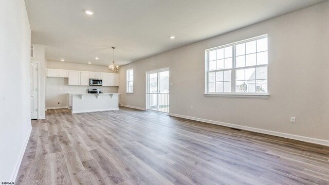 unfurnished living room featuring an inviting chandelier and light hardwood / wood-style flooring