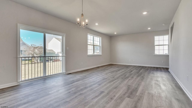 unfurnished room featuring a notable chandelier, a healthy amount of sunlight, and wood-type flooring