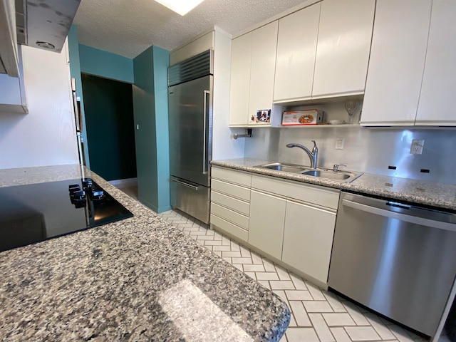 kitchen featuring white cabinetry, sink, light stone counters, a textured ceiling, and appliances with stainless steel finishes