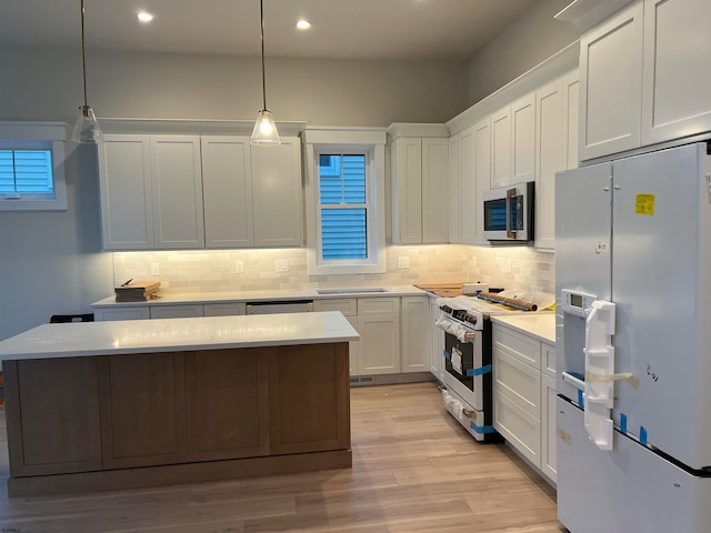 kitchen with white cabinets, hanging light fixtures, a center island, stainless steel appliances, and light wood-type flooring