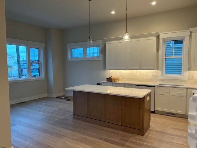 kitchen with a kitchen island, decorative light fixtures, white cabinets, backsplash, and light hardwood / wood-style flooring