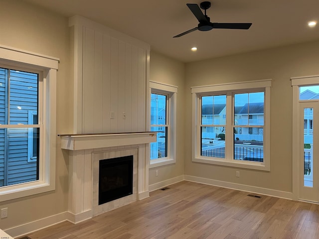 unfurnished living room with a tile fireplace, ceiling fan, and light hardwood / wood-style flooring