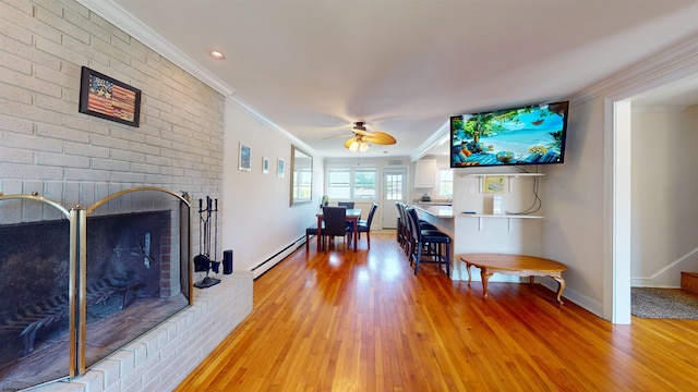 living room featuring ceiling fan, crown molding, a baseboard heating unit, a fireplace, and hardwood / wood-style floors