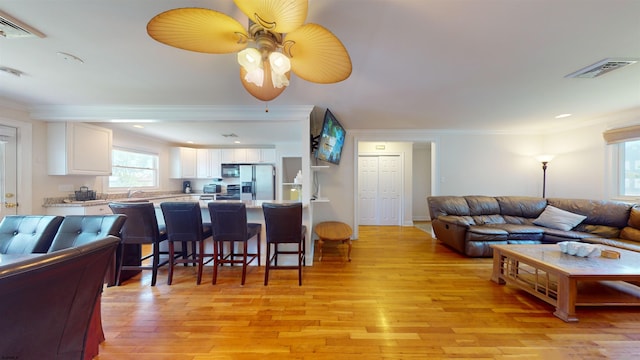 living room with light wood-type flooring, ceiling fan, and crown molding