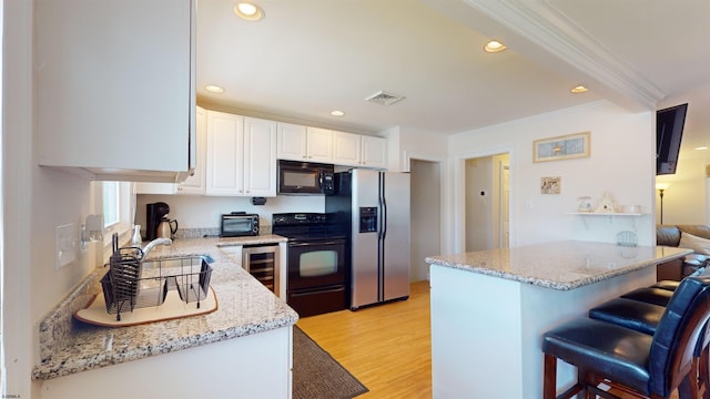 kitchen featuring white cabinetry, light hardwood / wood-style flooring, a breakfast bar area, black appliances, and ornamental molding