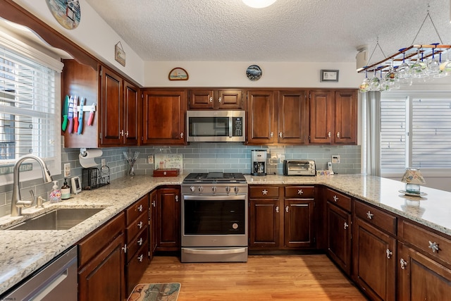 kitchen with light stone countertops, sink, a textured ceiling, appliances with stainless steel finishes, and light wood-type flooring