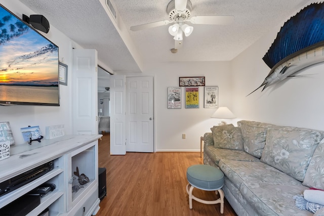 living room featuring ceiling fan, a textured ceiling, and light hardwood / wood-style flooring