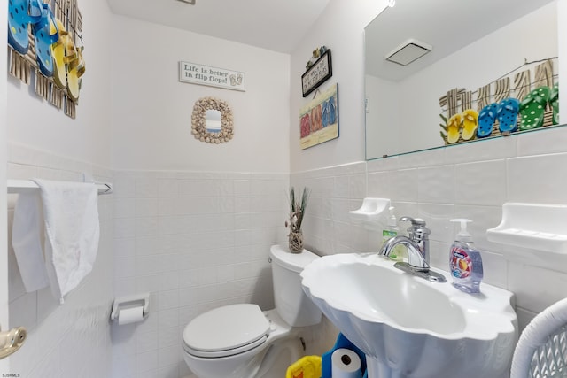 bathroom featuring toilet, tile walls, and sink