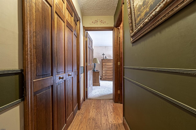 hall with a textured ceiling and light hardwood / wood-style flooring