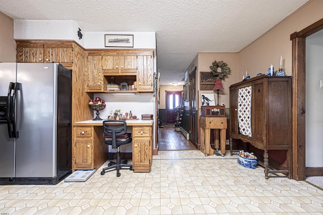 kitchen with stainless steel fridge, light wood-type flooring, a textured ceiling, and built in desk