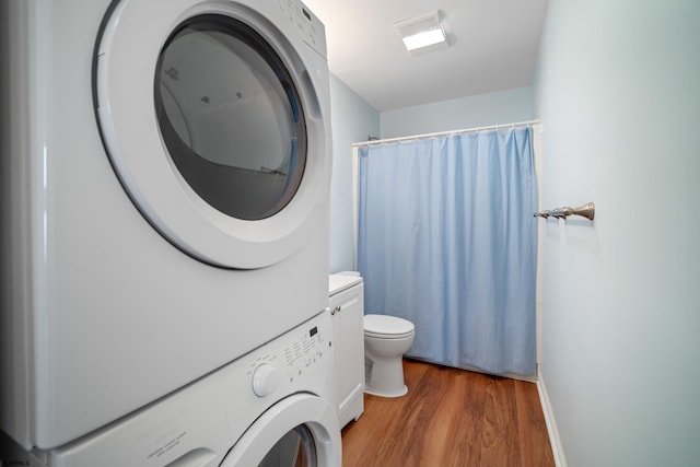 bathroom featuring wood-type flooring, vanity, stacked washing maching and dryer, and toilet