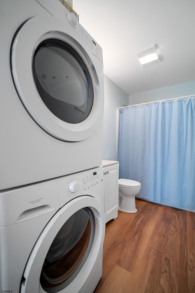 washroom with hardwood / wood-style flooring and stacked washer / dryer