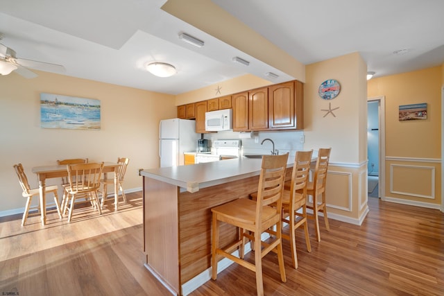 kitchen with kitchen peninsula, ceiling fan, light hardwood / wood-style flooring, and white appliances