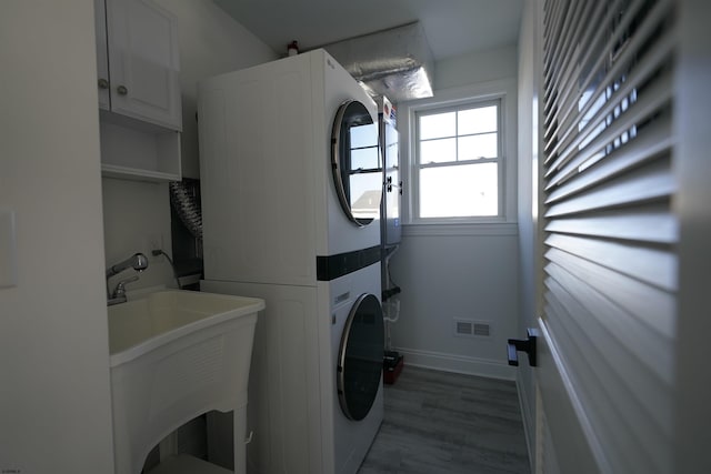 laundry area with stacked washer / drying machine, dark wood-type flooring, sink, and cabinets