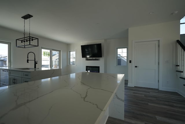 kitchen featuring white cabinetry, a large fireplace, hanging light fixtures, light stone countertops, and sink