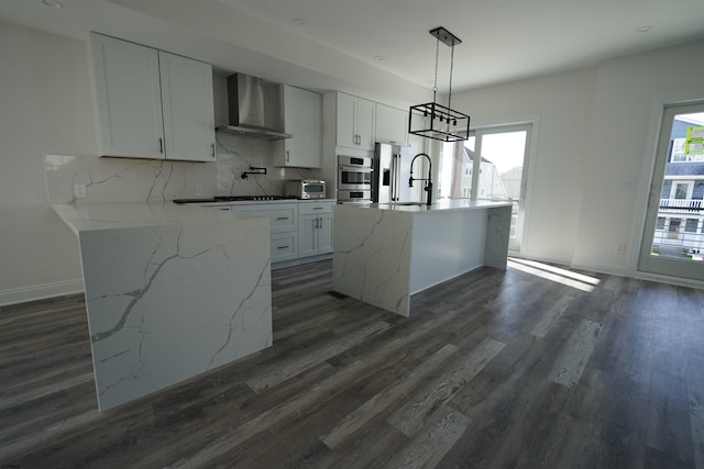 kitchen with backsplash, a kitchen island with sink, hanging light fixtures, wall chimney exhaust hood, and white cabinets