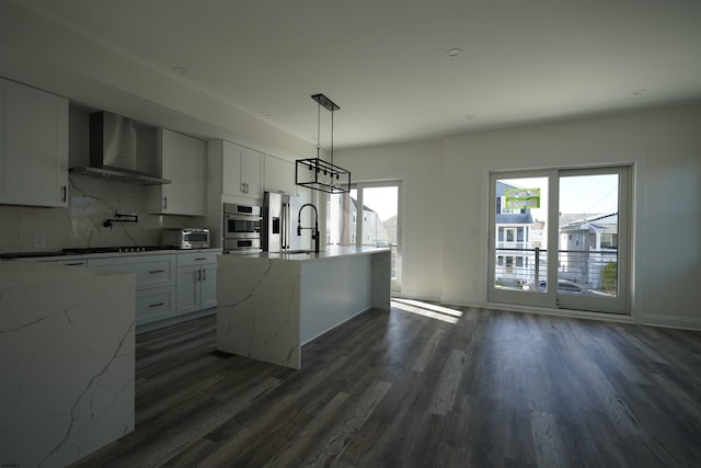 kitchen featuring hanging light fixtures, decorative backsplash, wall chimney range hood, and white cabinetry