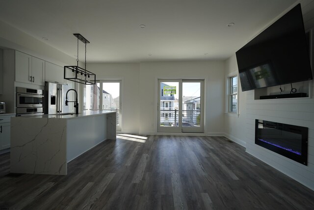 kitchen with white cabinetry, hanging light fixtures, light stone countertops, appliances with stainless steel finishes, and dark hardwood / wood-style flooring