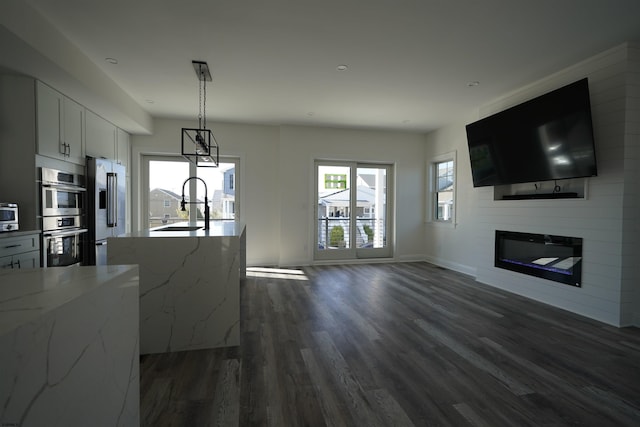 kitchen with white cabinetry, appliances with stainless steel finishes, a fireplace, light stone counters, and sink