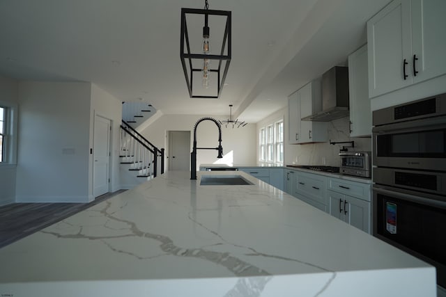 kitchen with a center island with sink, sink, white cabinetry, appliances with stainless steel finishes, and wall chimney exhaust hood