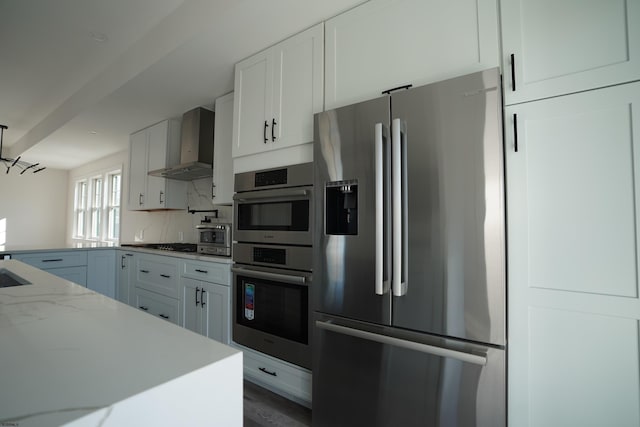 kitchen featuring tasteful backsplash, white cabinets, wall chimney exhaust hood, and stainless steel appliances