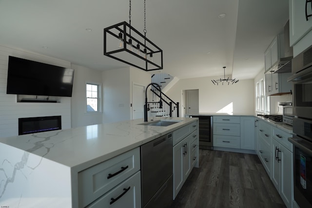 kitchen with a center island with sink, stainless steel appliances, decorative light fixtures, a large fireplace, and sink