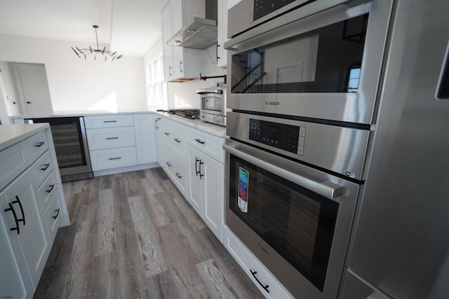 kitchen with an inviting chandelier, light hardwood / wood-style flooring, white cabinets, wall chimney exhaust hood, and beverage cooler