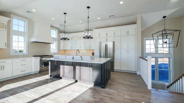 kitchen featuring dark hardwood / wood-style flooring, premium range hood, stainless steel appliances, decorative light fixtures, and a center island with sink