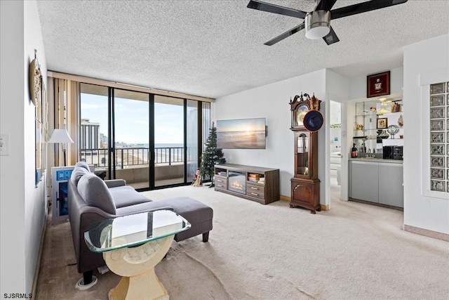 living room with ceiling fan, light carpet, a textured ceiling, and a wall of windows