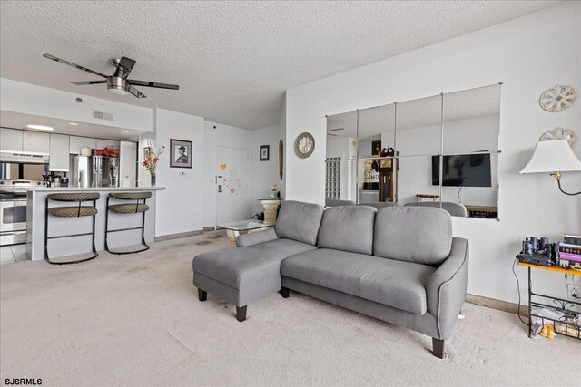 living room with light carpet, ceiling fan, and a textured ceiling