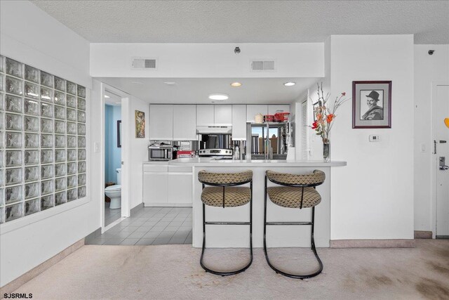 kitchen featuring carpet, a textured ceiling, stainless steel appliances, and white cabinetry