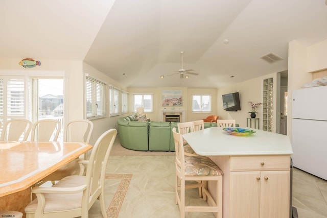 kitchen featuring a tile fireplace, vaulted ceiling, ceiling fan, light brown cabinetry, and white fridge