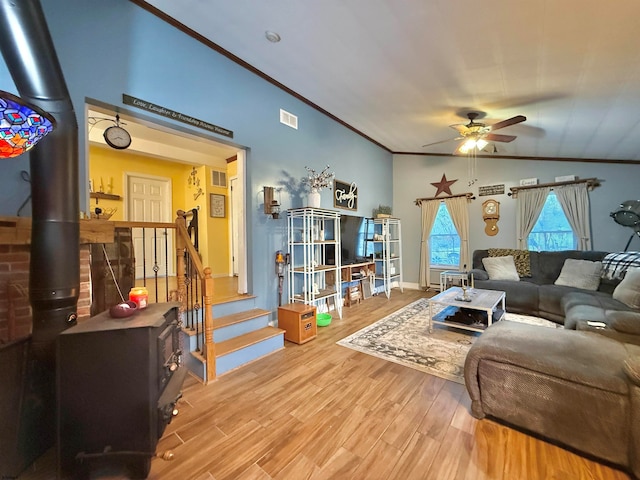 living room with ornamental molding, vaulted ceiling, ceiling fan, hardwood / wood-style flooring, and a wood stove