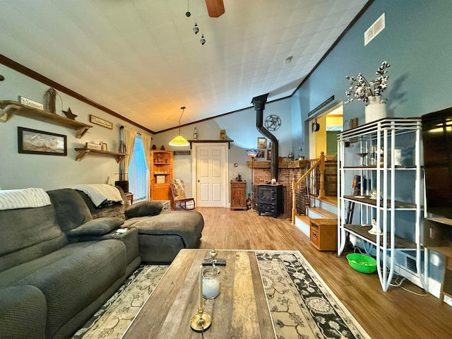 living room with a wood stove, crown molding, vaulted ceiling, ceiling fan, and wood-type flooring